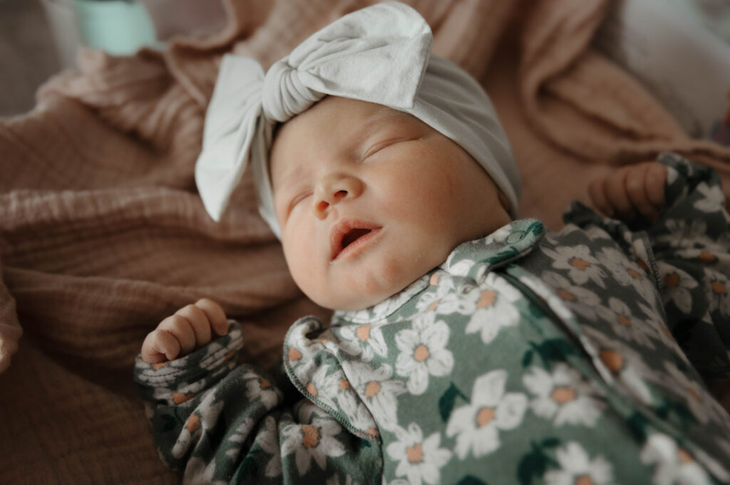 Newborn baby sleeping in bed with a bow on her head showing baby-led posing
