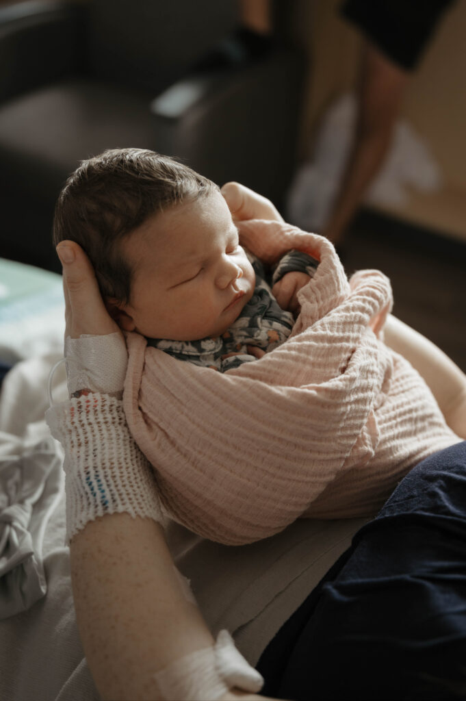 Newborn baby-led posing where baby is lightly swaddled in mom's arms in the hospital.